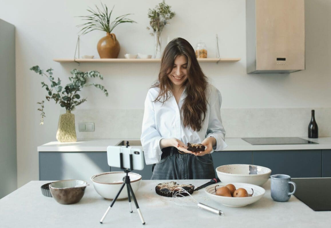 A girl posting a cooking video to social media standing in front of a smartphone on tripod